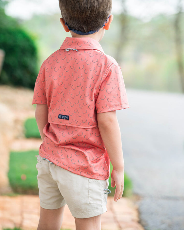 Child wearing a red patterned shirt and beige shorts outdoors