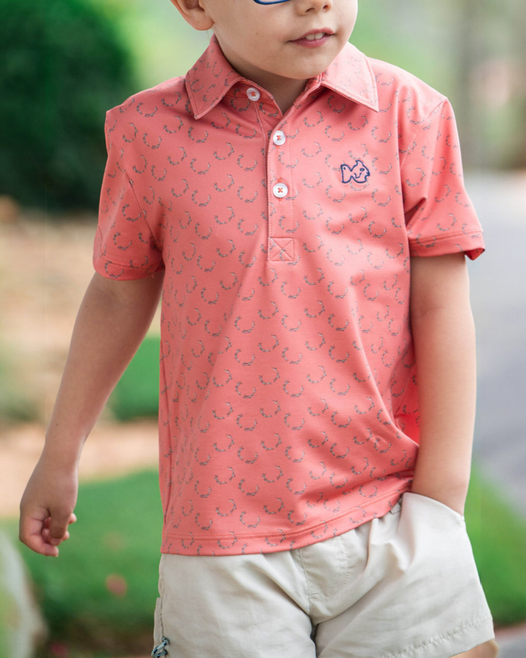 Child wearing a pink patterned polo shirt with a logo outdoors