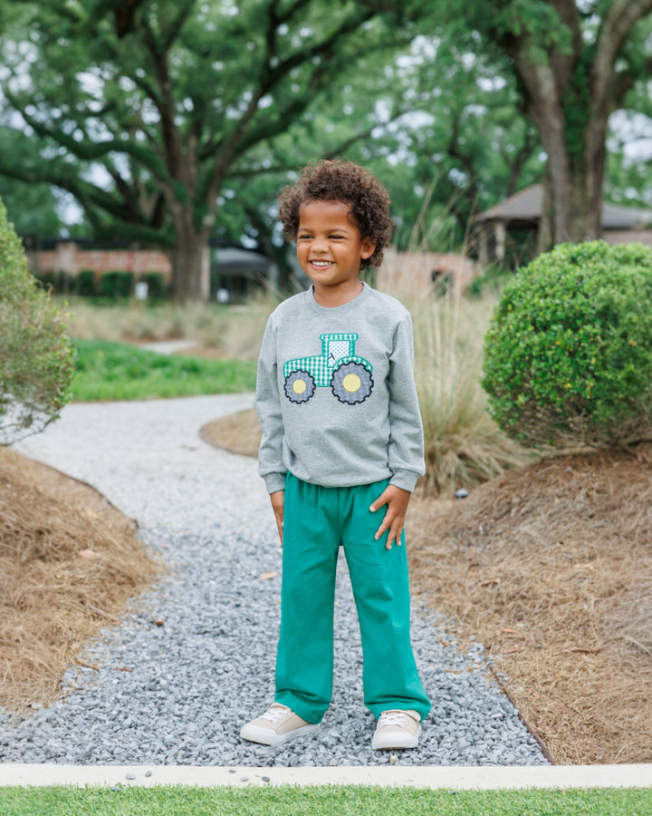 Child wearing a gray sweatshirt with a colorful design and green pants standing on a gravel path.
