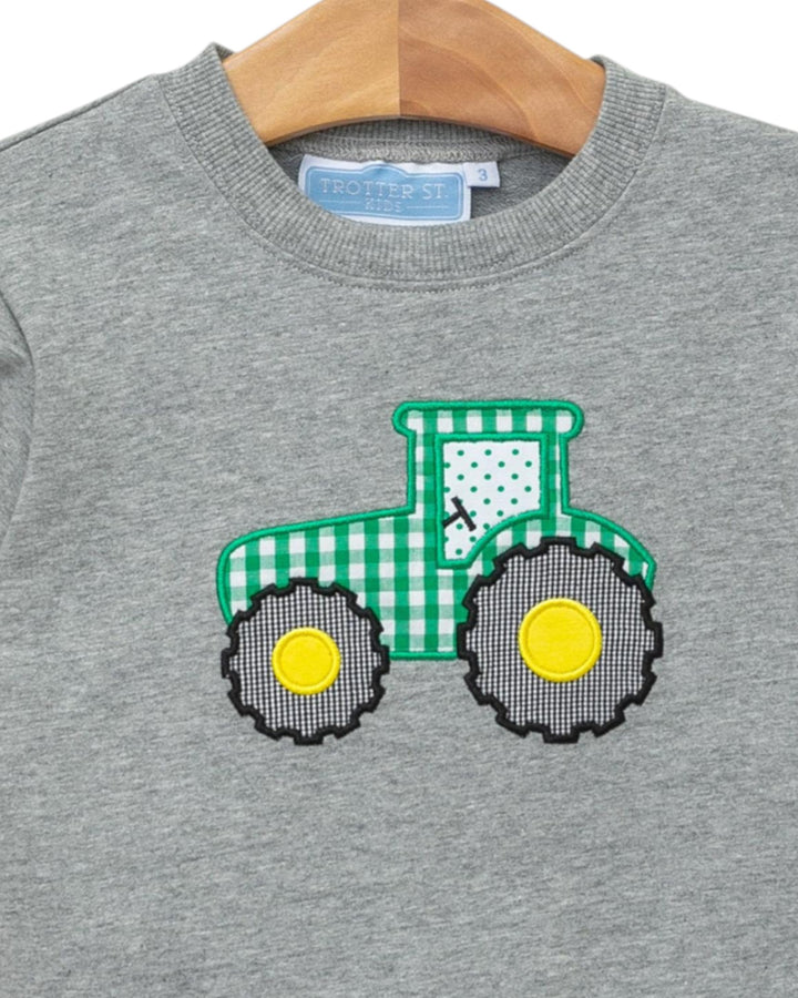 Gray sweatshirt with a green and yellow tractor design on a wooden hanger
