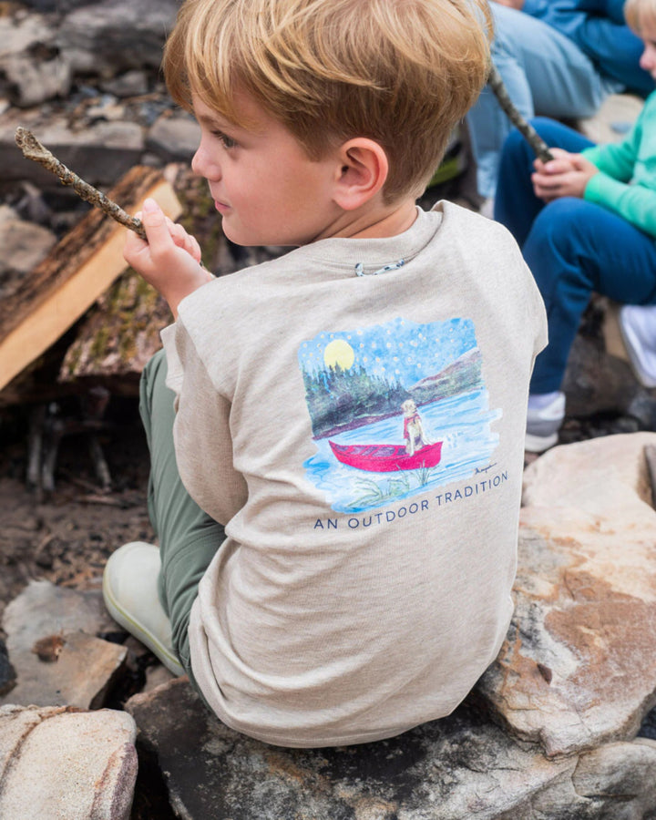 Child wearing a shirt with a nature-themed design, sitting on rocks outdoors.