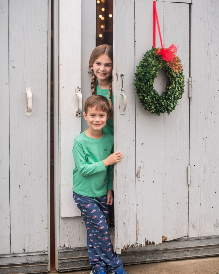 Two children standing in a wooden door frame with a wreath on a white wall.