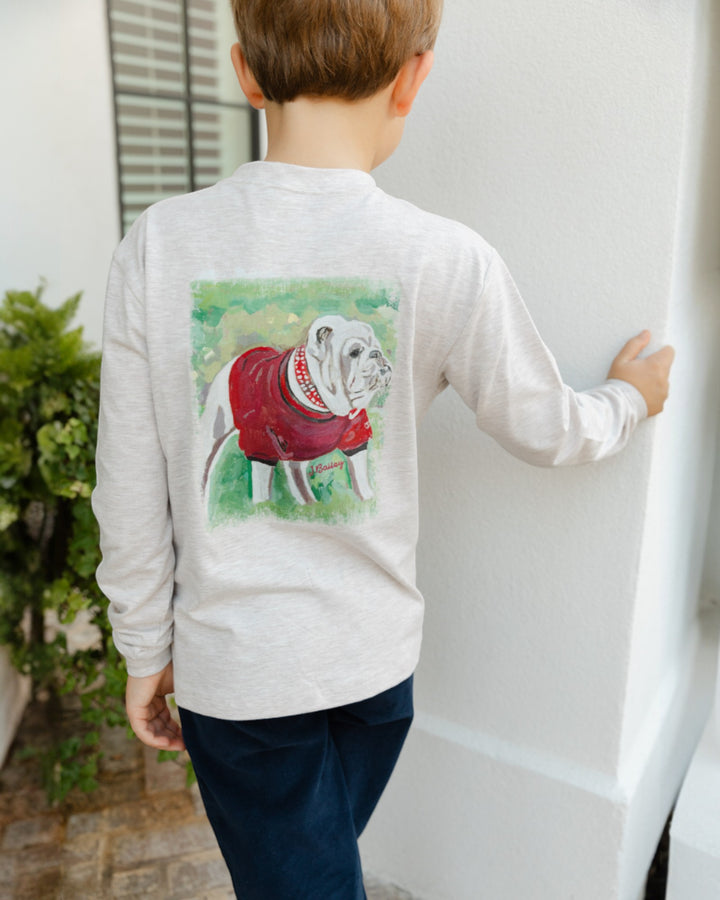 Child wearing a tee with a dog graphic on the back, standing against a white wall.