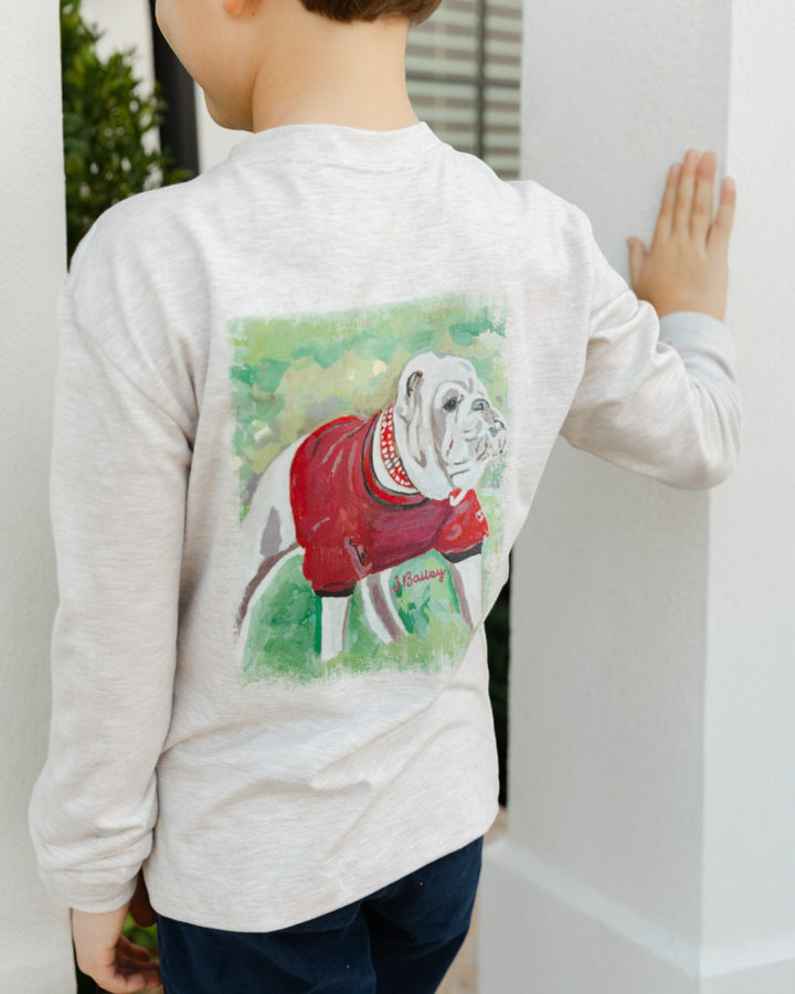 Child wearing a long-sleeve shirt with a dog graphic on the back, standing against a white wall.