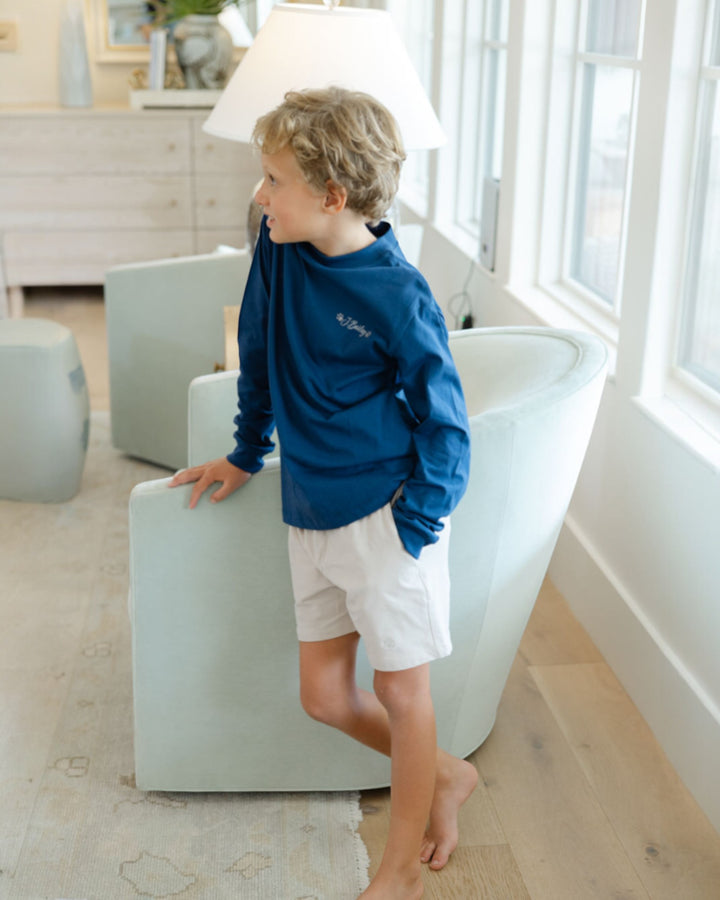 Child in a blue shirt and white shorts standing in a modern living room.