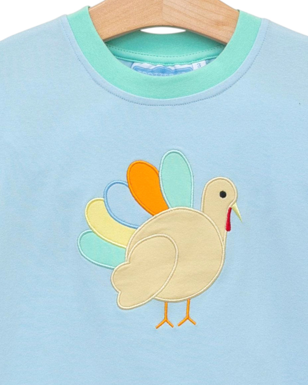 Light blue shirt with a colorful turkey applique on a hanger