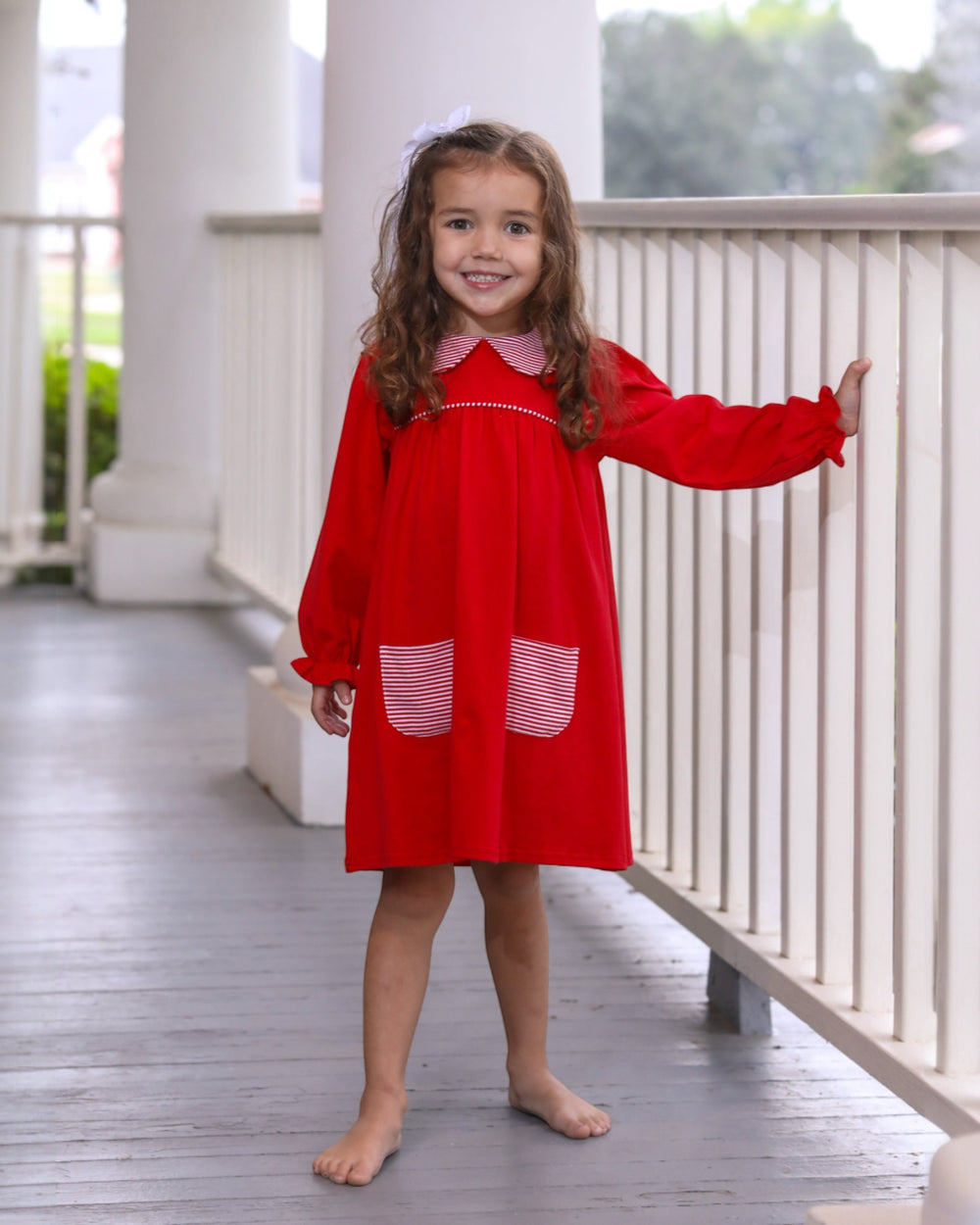 Young girl in a red dress standing on a wooden deck.