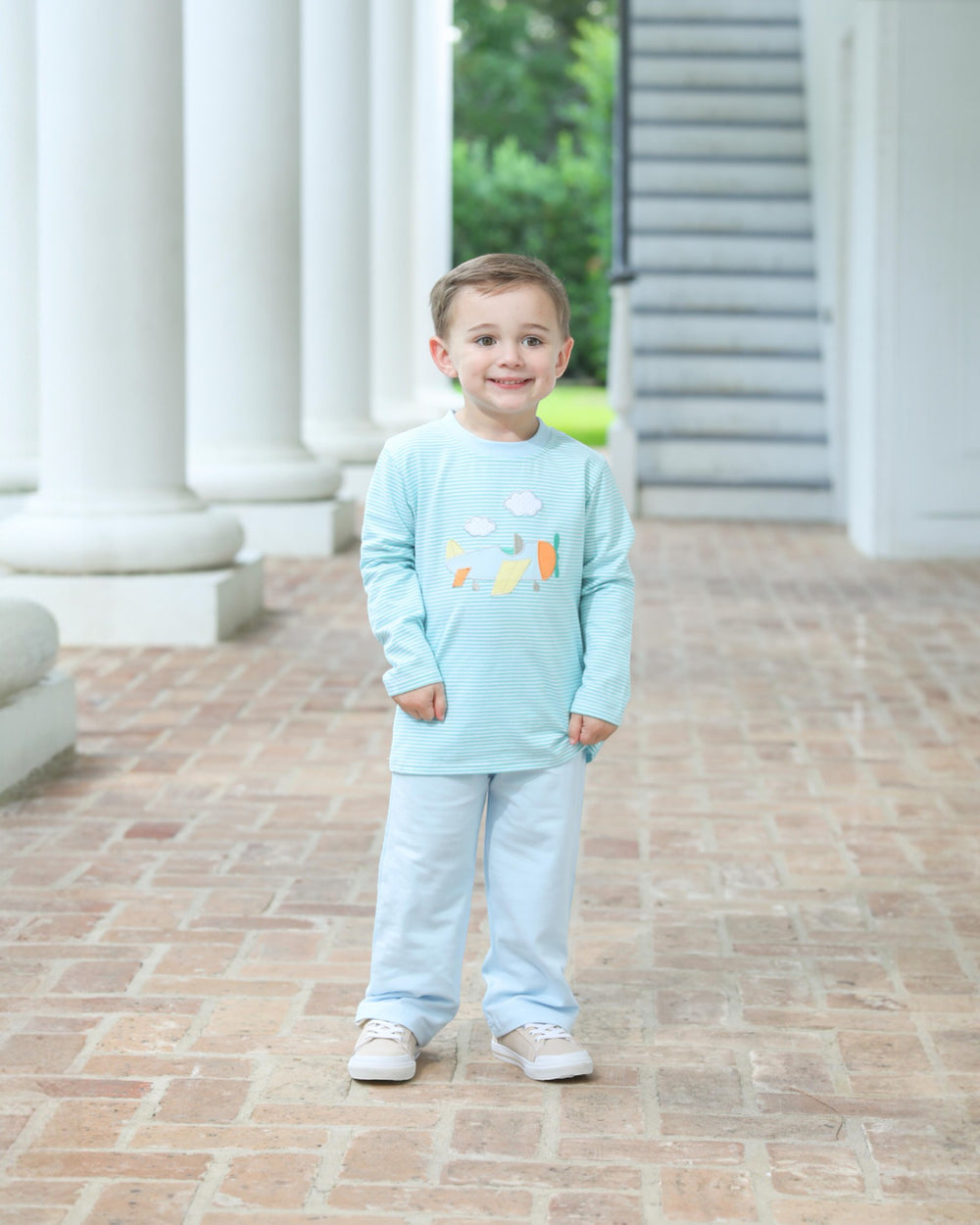 Child wearing a light blue outfit with colorful designs standing on a brick path.