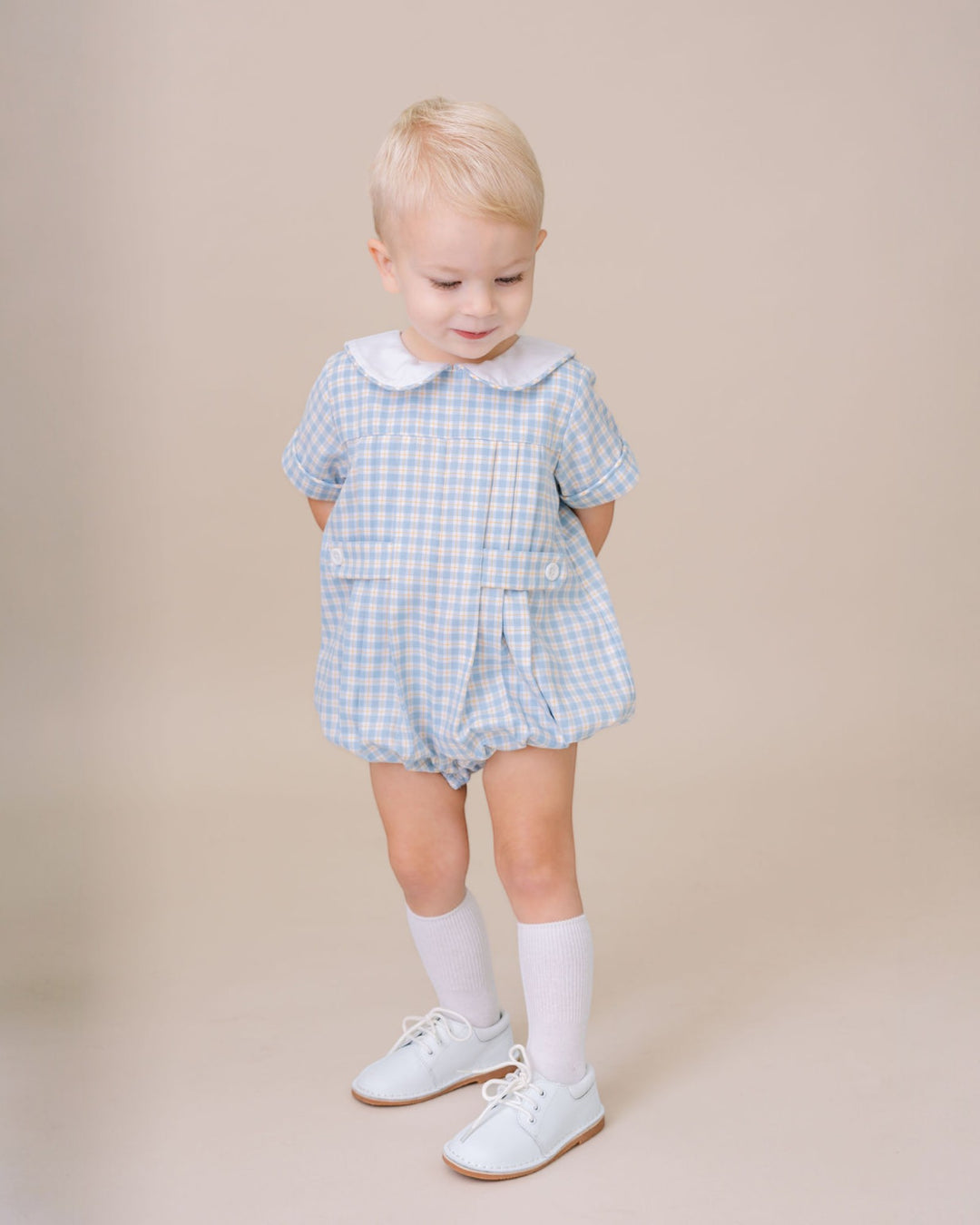 Child wearing a blue checkered outfit with a white collar on a beige background