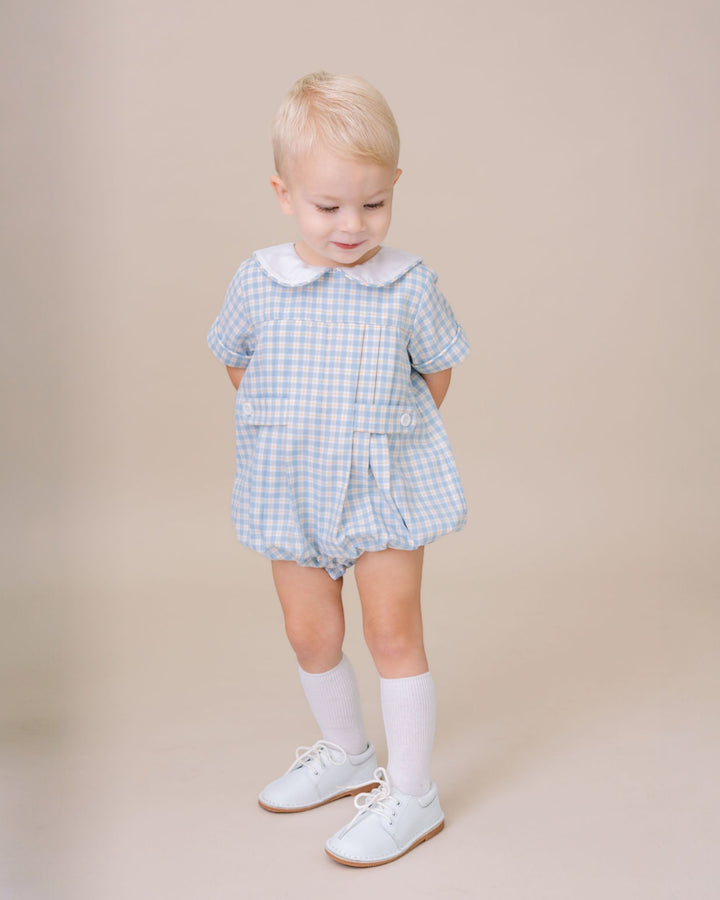 Child wearing a blue checkered outfit with a white collar on a beige background