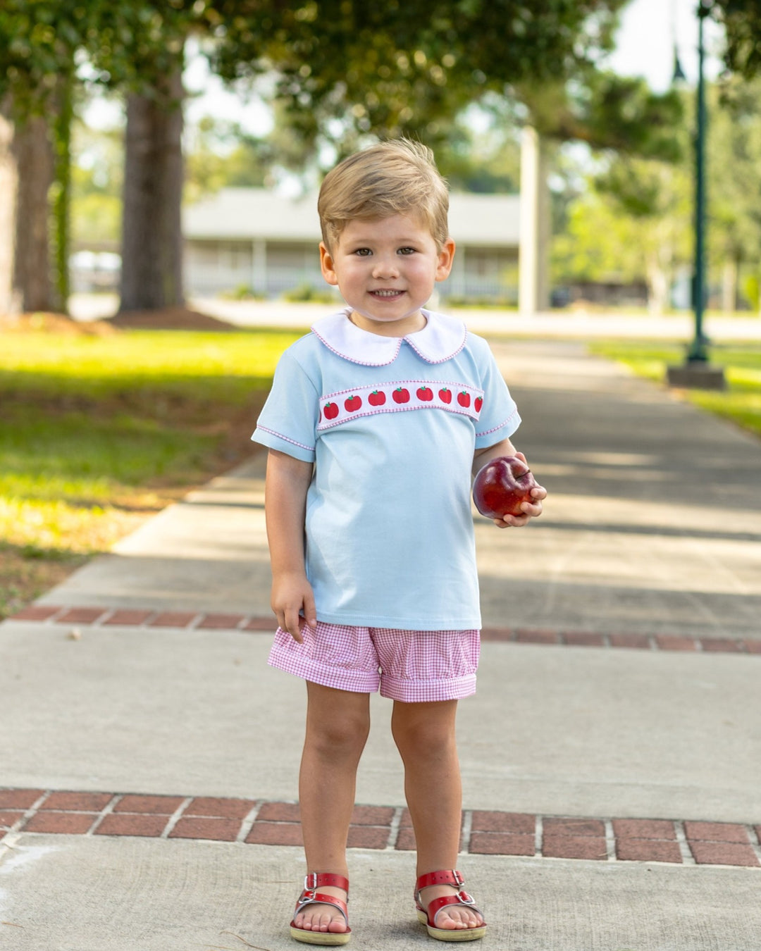 Child in light blue shirt with red polka dots and pink shorts standing on a paved path.