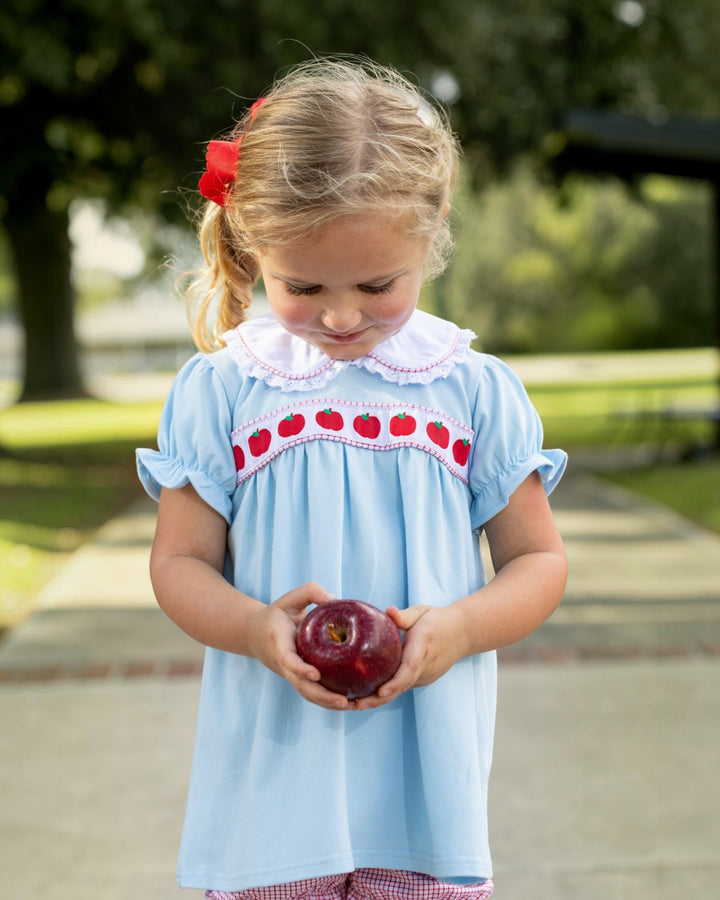 Young girl holding an apple outdoors in a park-like setting