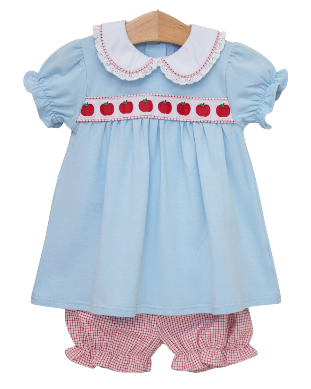 Light blue dress with red apple pattern and pink checkered shorts on a white background
