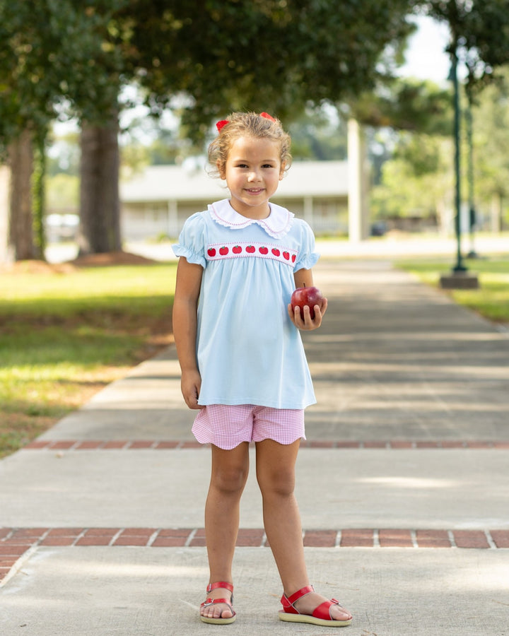 Young girl holding an apple on a paved path with trees in the background