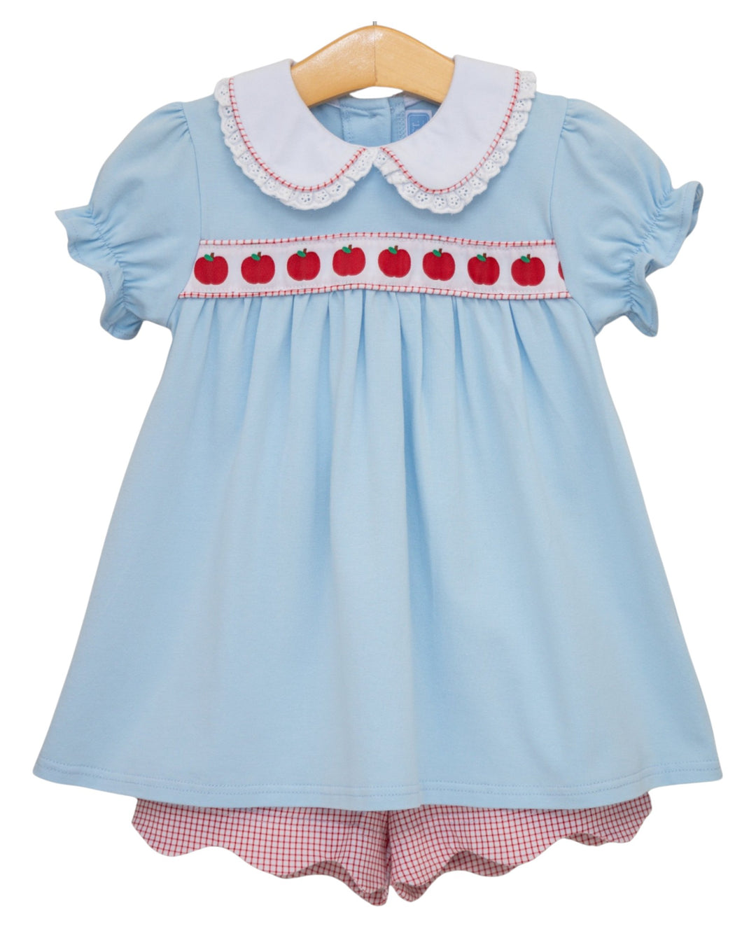 Light blue dress with red apple design and checkered shorts on a hanger