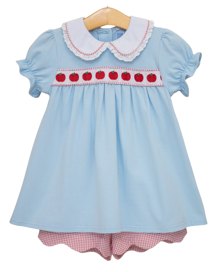Light blue dress with red apple design and checkered shorts on a hanger