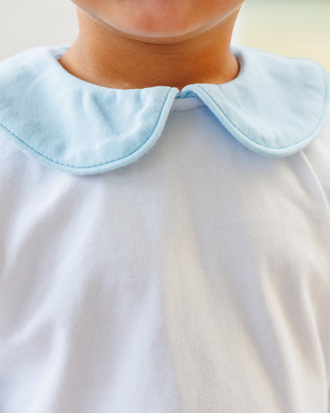 Close-up of a child wearing a white top with a light blue Peter Pan collar.