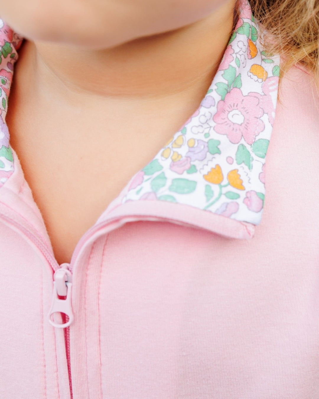 Close-up of a child wearing a pink zip-up jacket with a white collar featuring a pastel pink, green, and orange floral pattern, that store
