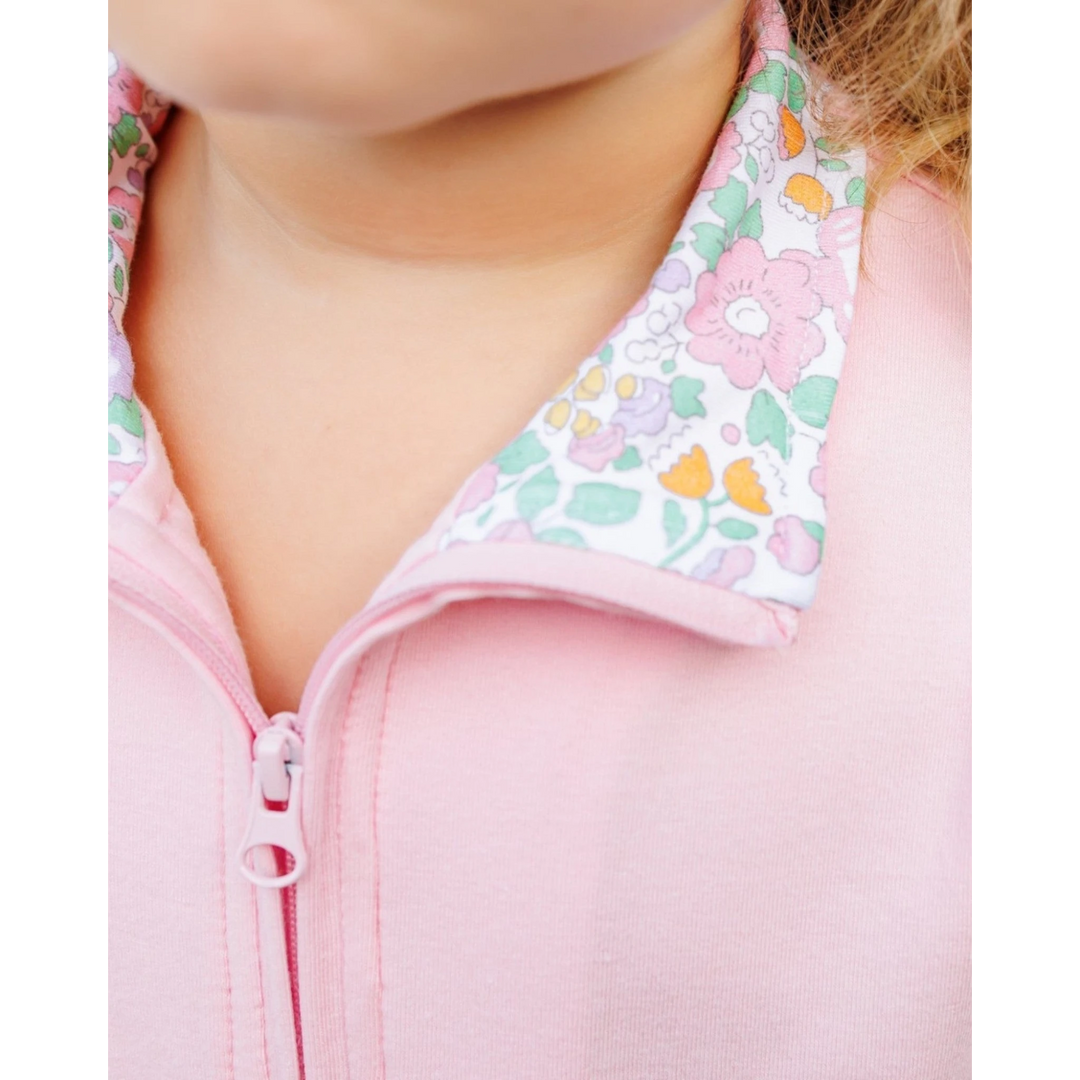 Close-up of a child wearing a pink zip-up jacket with a white collar featuring a pastel pink, green, and orange floral pattern, that store