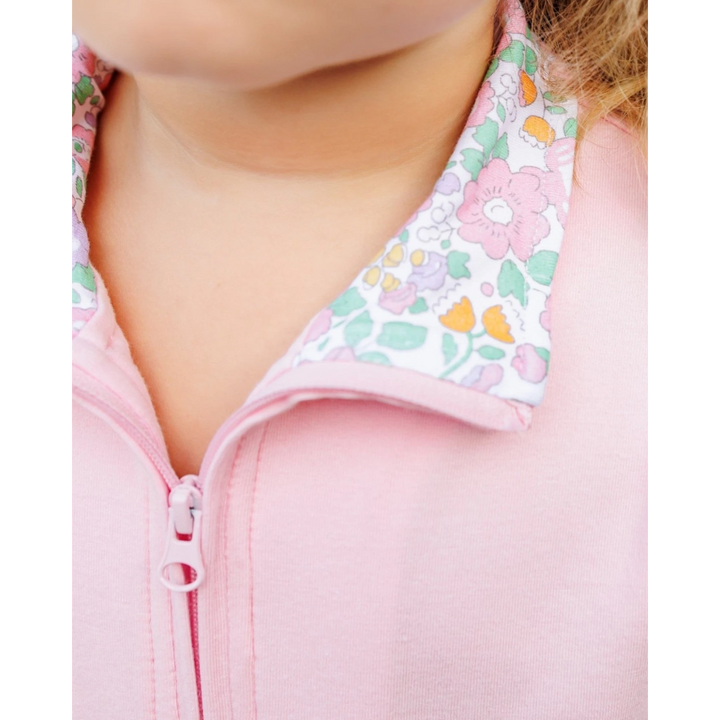 Close-up of a child wearing a pink zip-up jacket with a white collar featuring a pastel pink, green, and orange floral pattern, that store