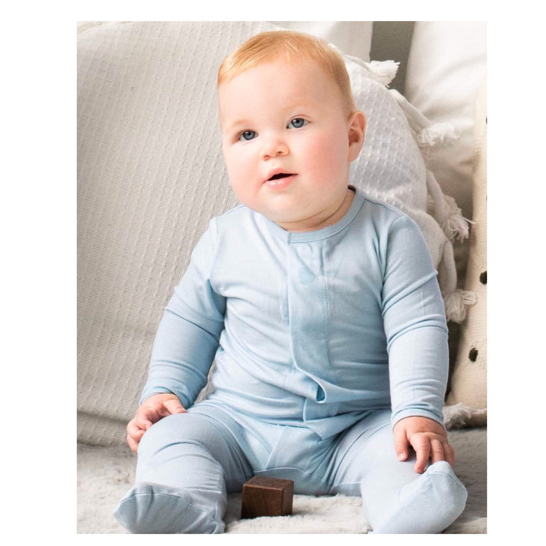 Baby in a light blue onesie sitting on a soft surface