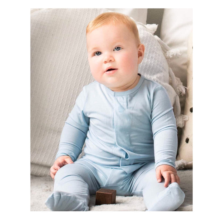 Baby in a light blue onesie sitting on a soft surface
