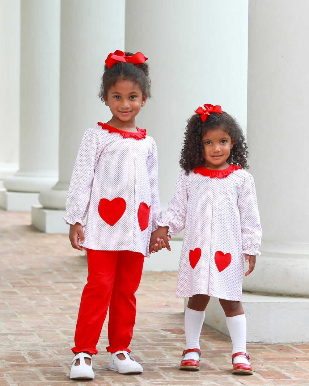 Two young girls in matching outfits with red hearts standing outdoors.
