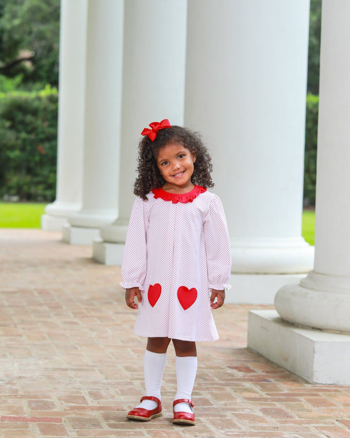 Young girl in a white dress with red hearts standing in front of classical columns.
