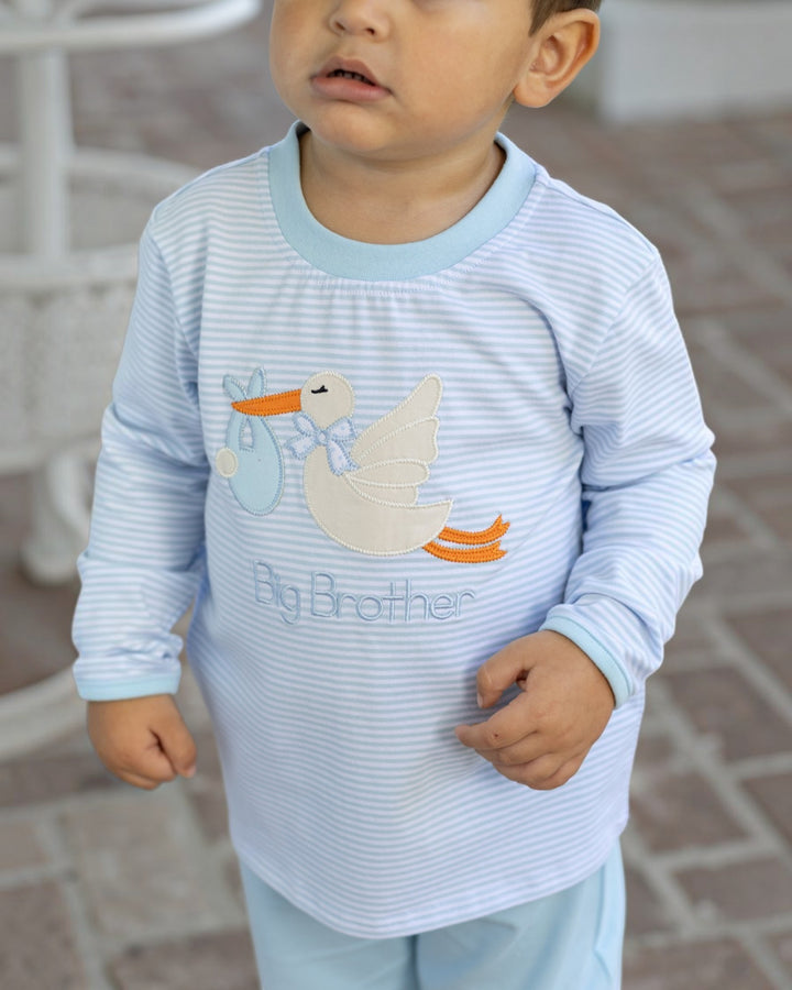 A toddler wearing a light blue and white striped long-sleeve shirt with a stork graphic and the words &