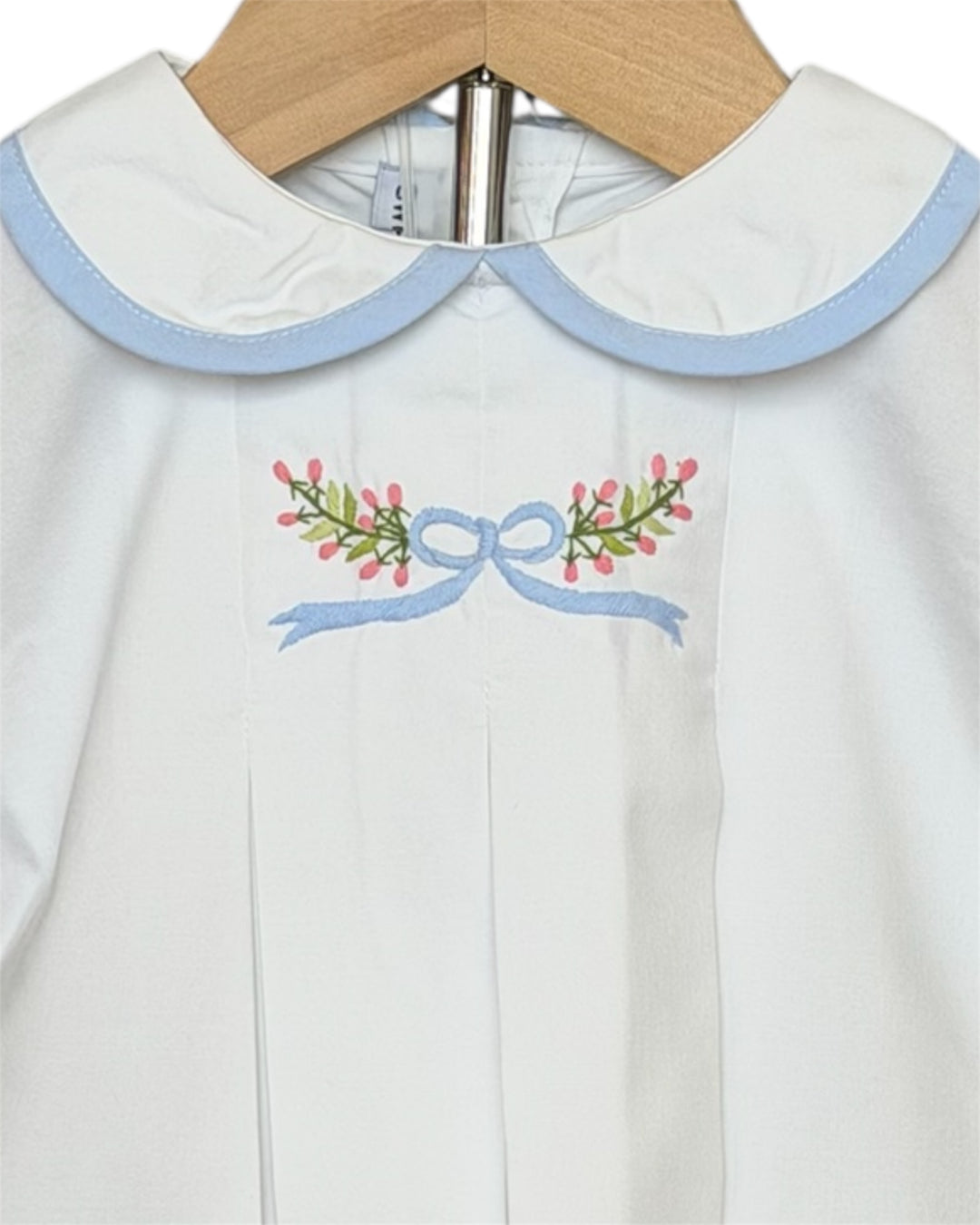 White dress with blue trim and floral embroidery on a hanger
