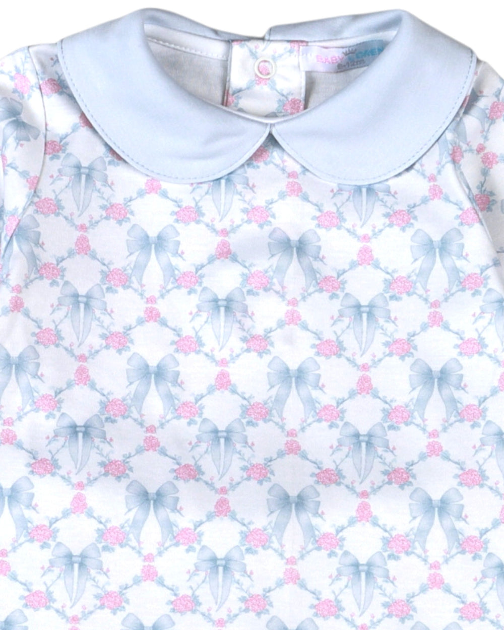 A close-up of a baby dress featuring a light blue Peter Pan collar and a white body printed with a repeating pattern of blue bows and pink roses, that store