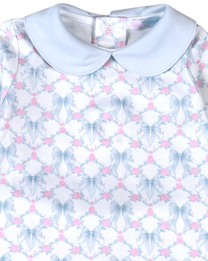 A close-up of a baby dress featuring a light blue Peter Pan collar and a white body printed with a repeating pattern of blue bows and pink roses, that store