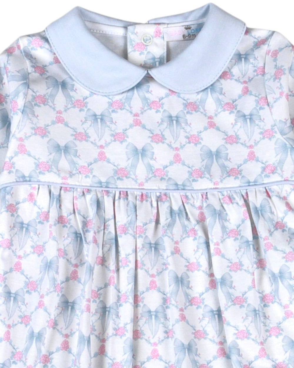 A close-up of a baby girl's dress featuring a light blue Peter Pan collar and a white fabric printed with a repeating pattern of blue bows and pink flowers, that store