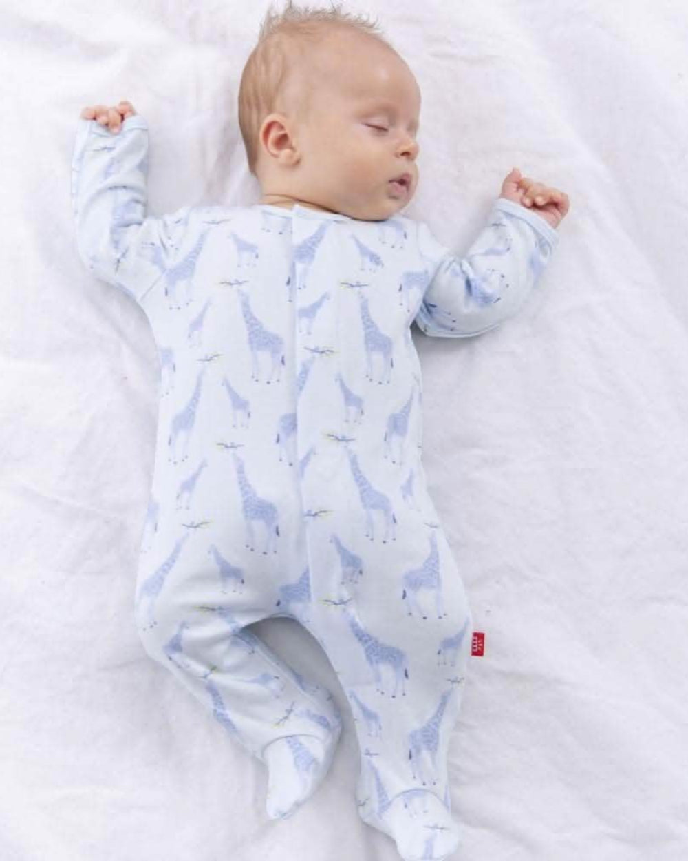 Baby wearing a blue and white patterned onesie lying on a white blanket