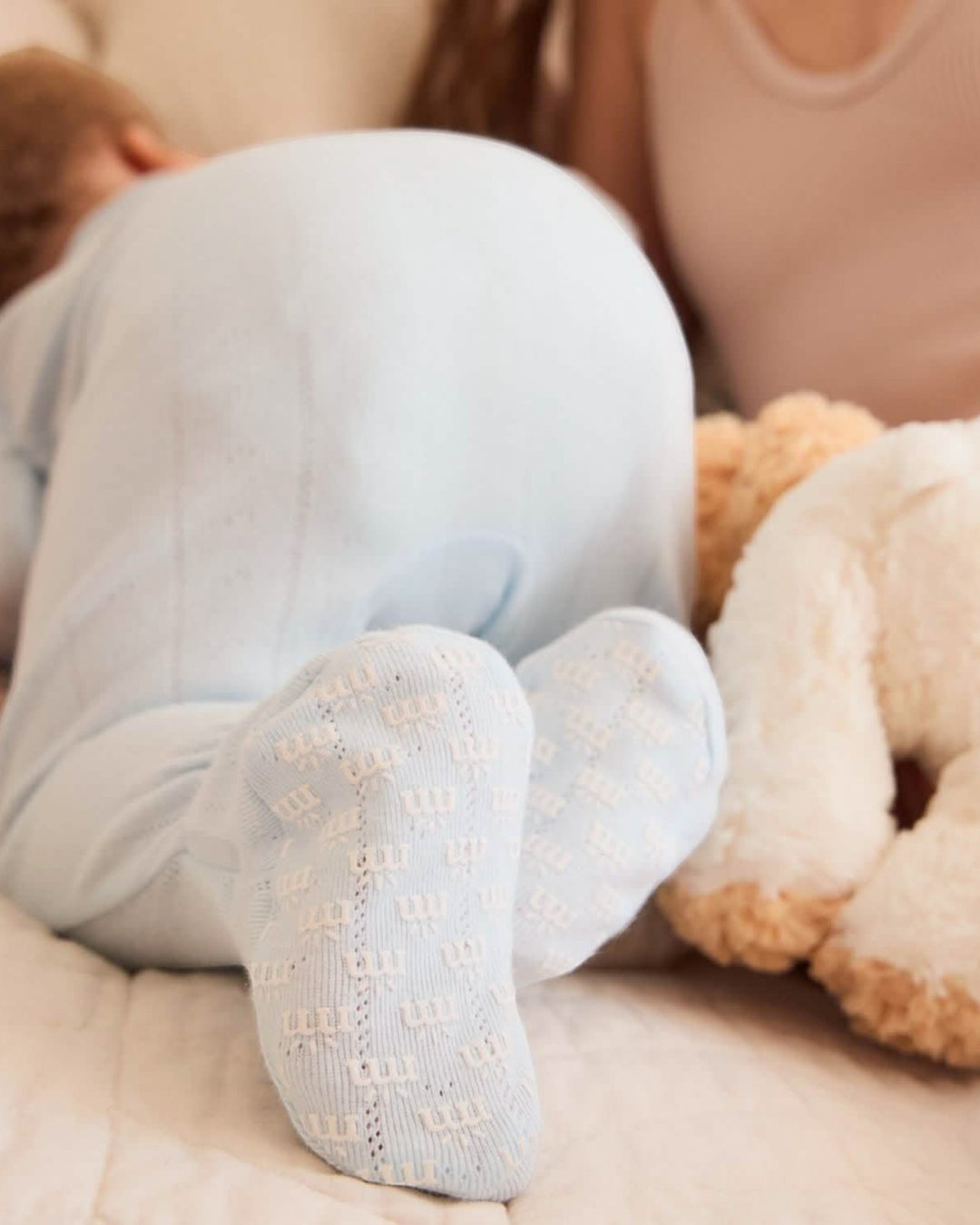 Baby wearing light blue socks with a teddy bear on a soft surface