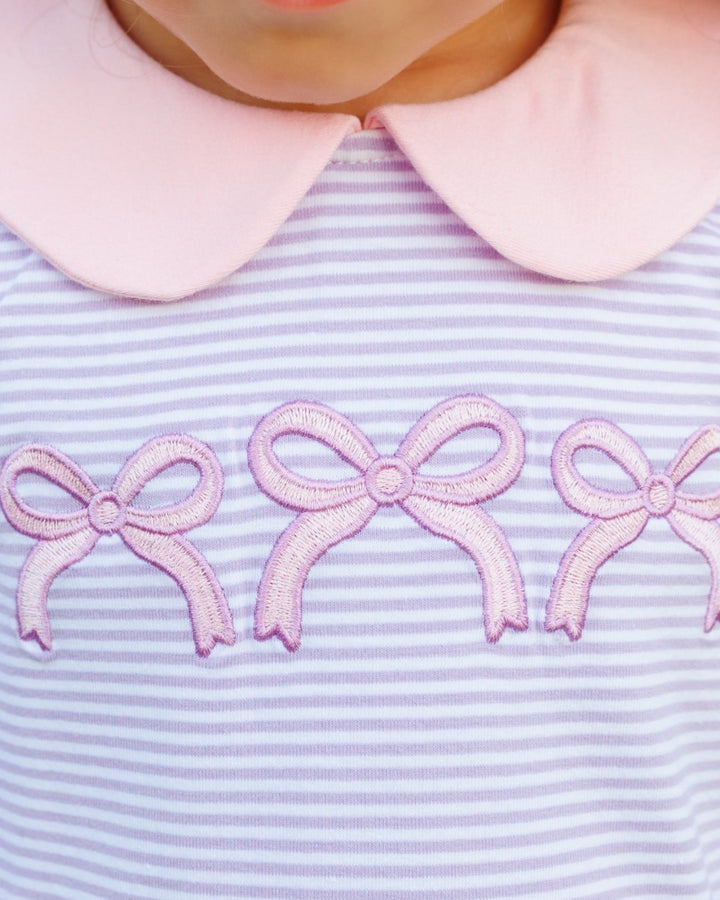 Close-up of a child wearing a light pink collar and a lavender and white striped top with three pink embroidered bows across the chest, that store