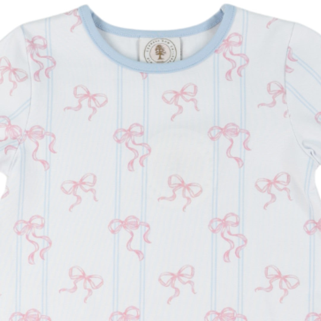 A close-up of a baby t-shirt featuring a white base with light blue vertical stripes and an all-over pink bow pattern. The shirt has a light blue crew neck and a small circular brand label inside the collar, that store