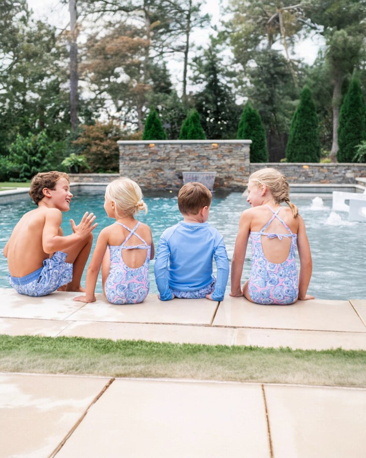 Four children sitting by a pool with trees in the background
