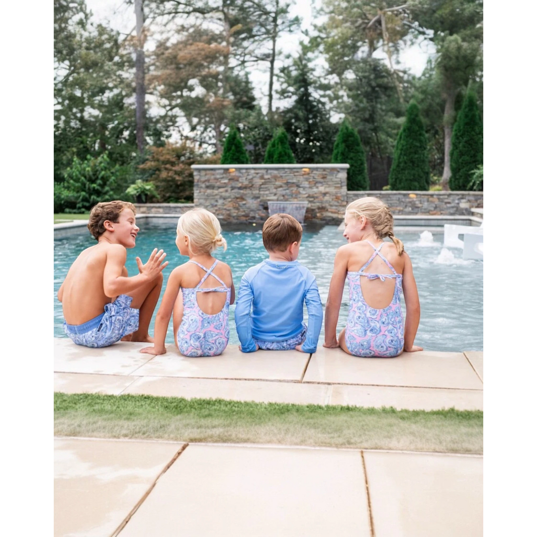 Four children sitting by a pool with trees in the background