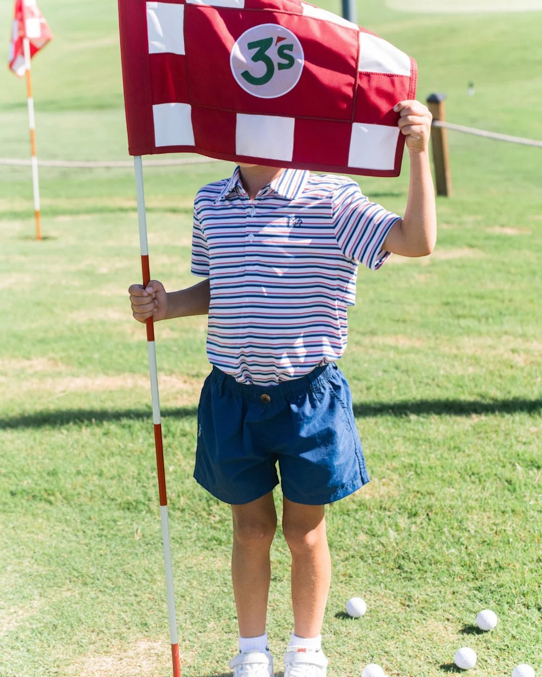 A child standing on a grassy golf course holding a red and white checkered flag with a green &
