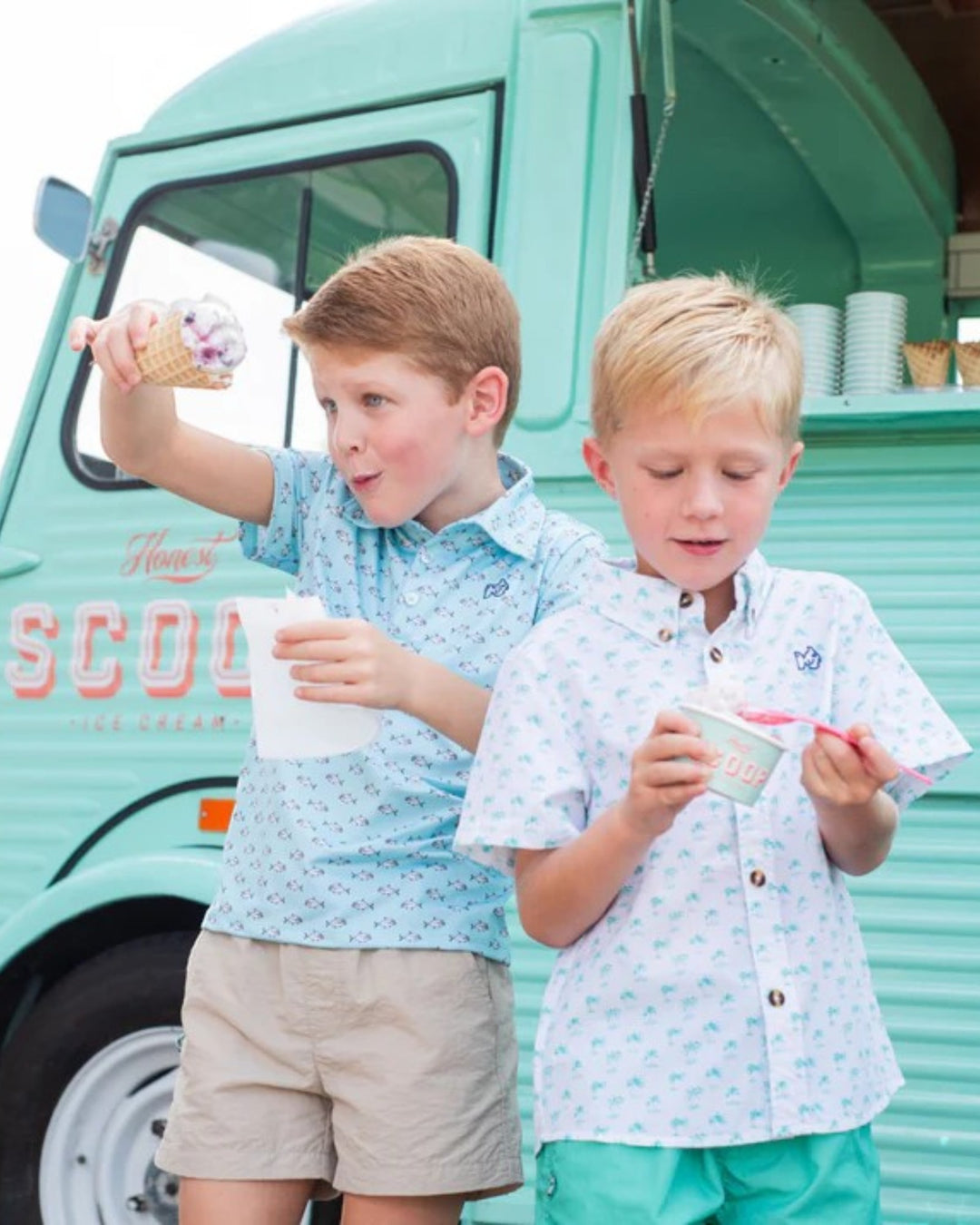Two children enjoying ice cream in front of a teal ice cream truck.