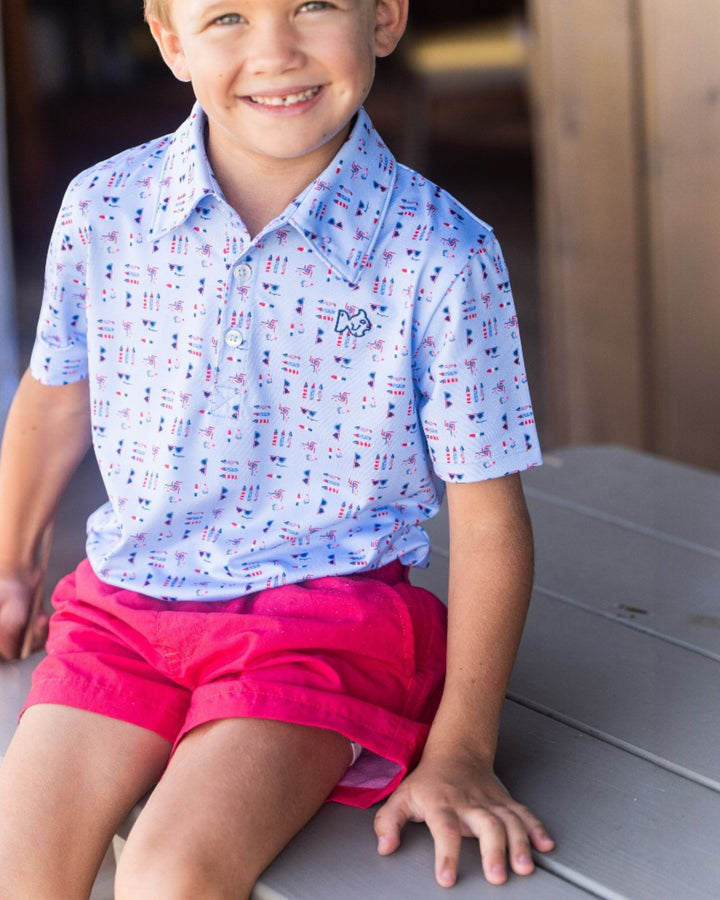 Child wearing a patterned blue shirt and pink shorts sitting on a surface.