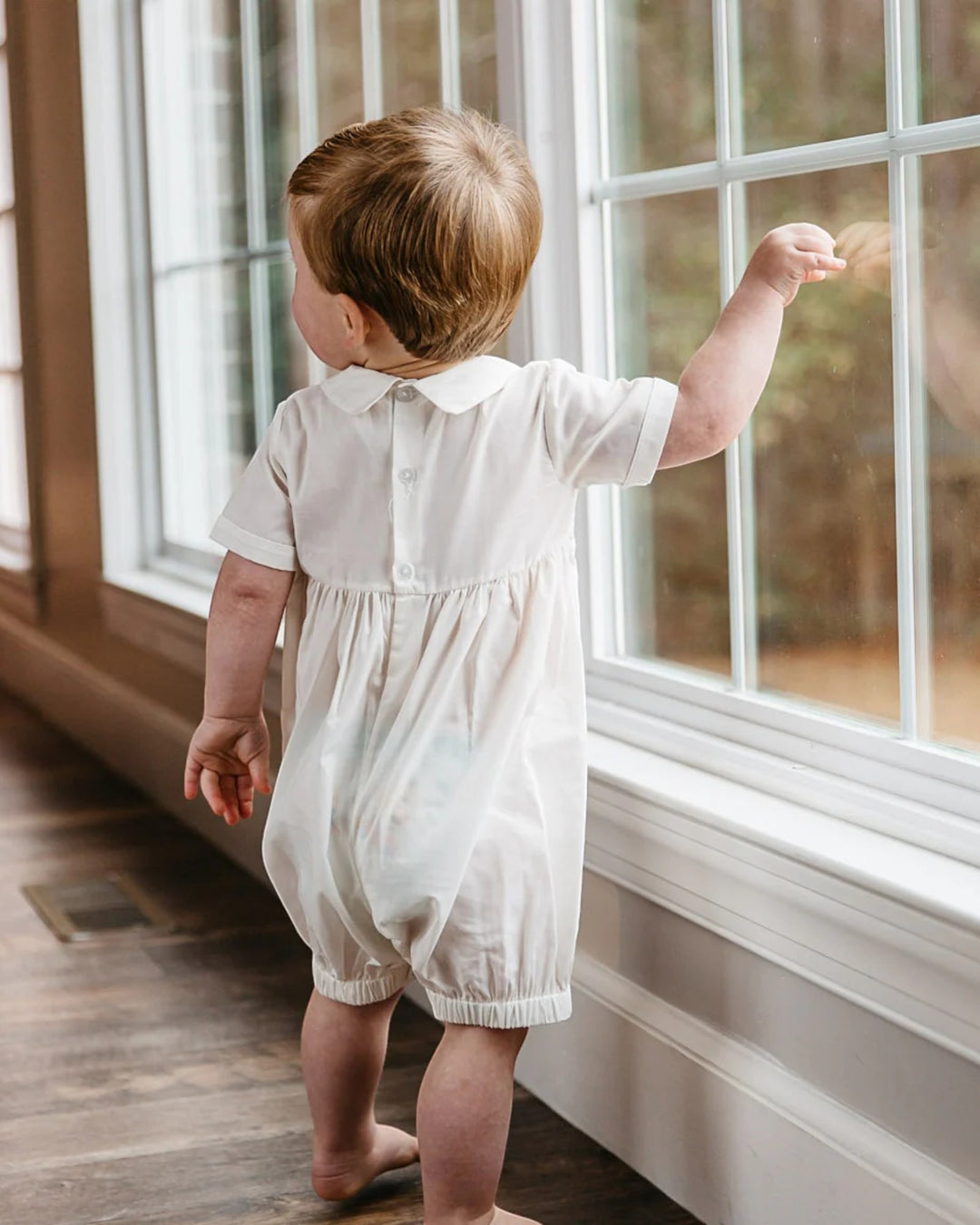 Child in a white romper standing by a window