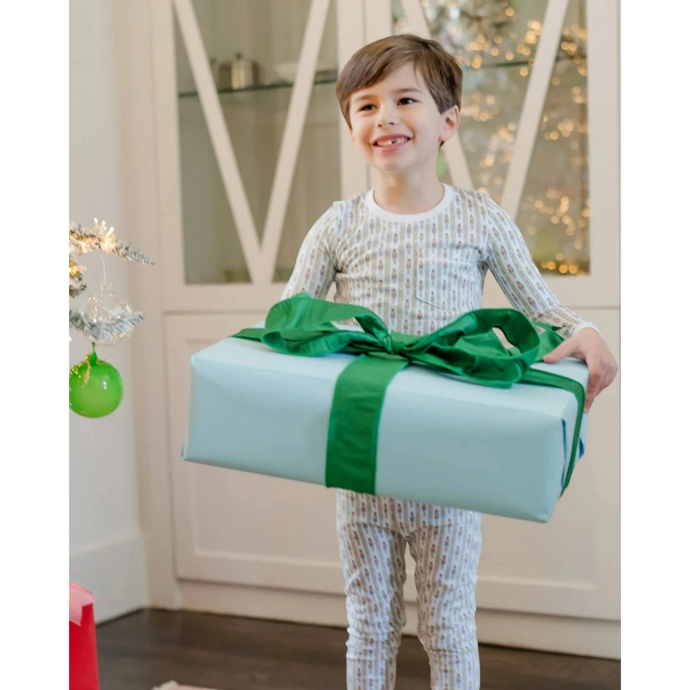 Child holding a large gift box with a green ribbon in a festive indoor setting.