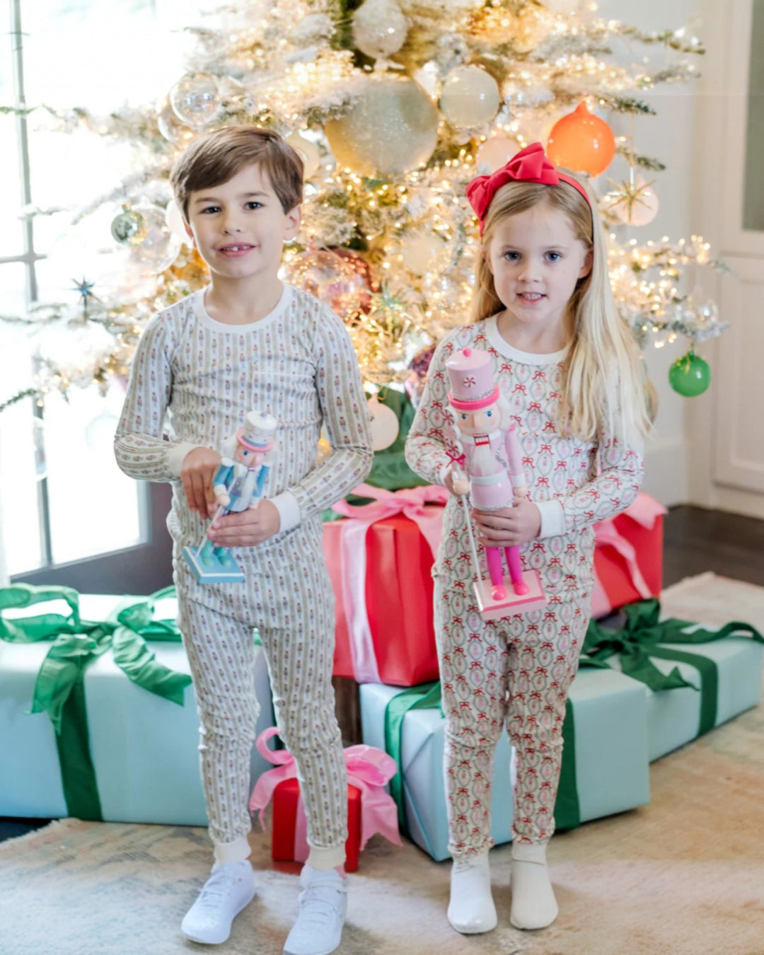 Two children in pajamas standing in front of a decorated Christmas tree with presents.