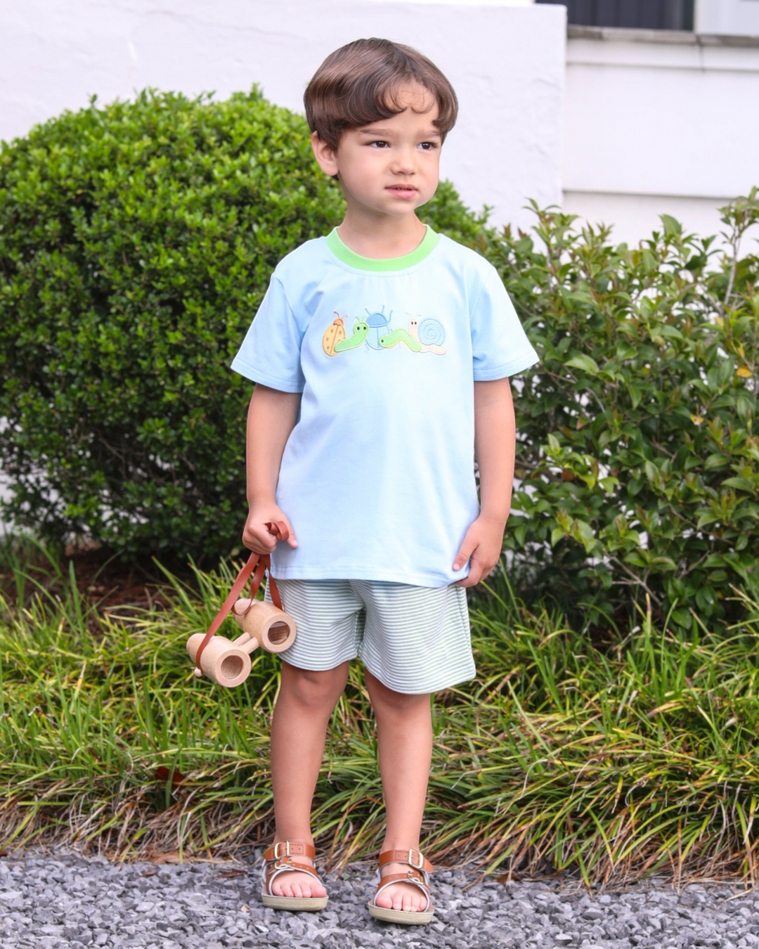 Child wearing a light blue shirt with cartoon characters and light gray shorts, standing outdoors.