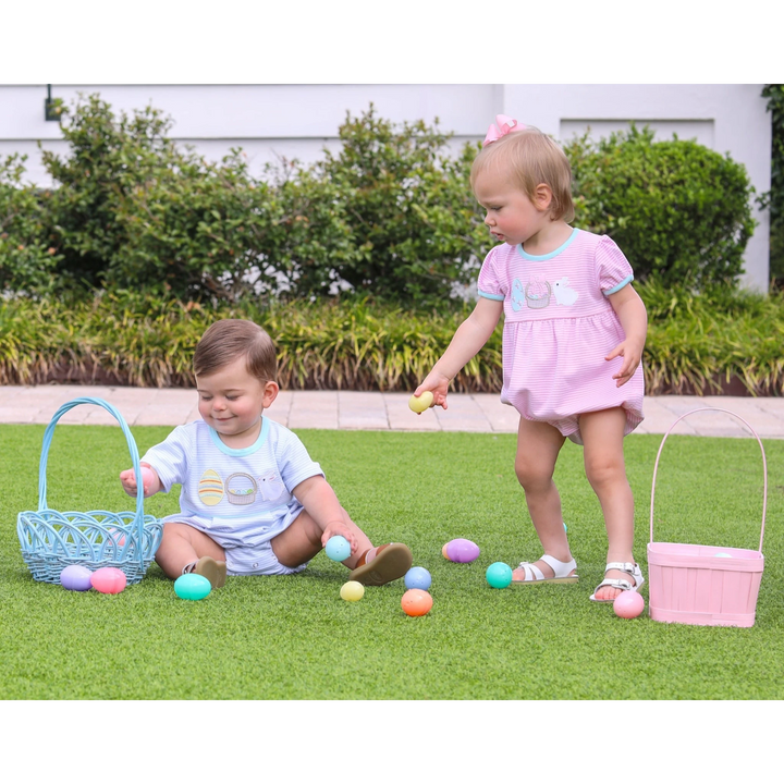 Two children playing with Easter eggs on a grassy lawn.