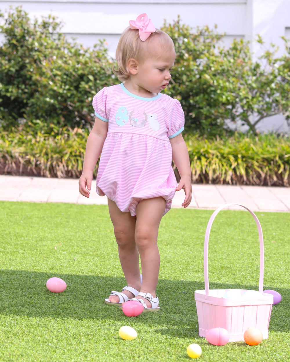 Child in a pink bubble playing with Easter eggs on grass