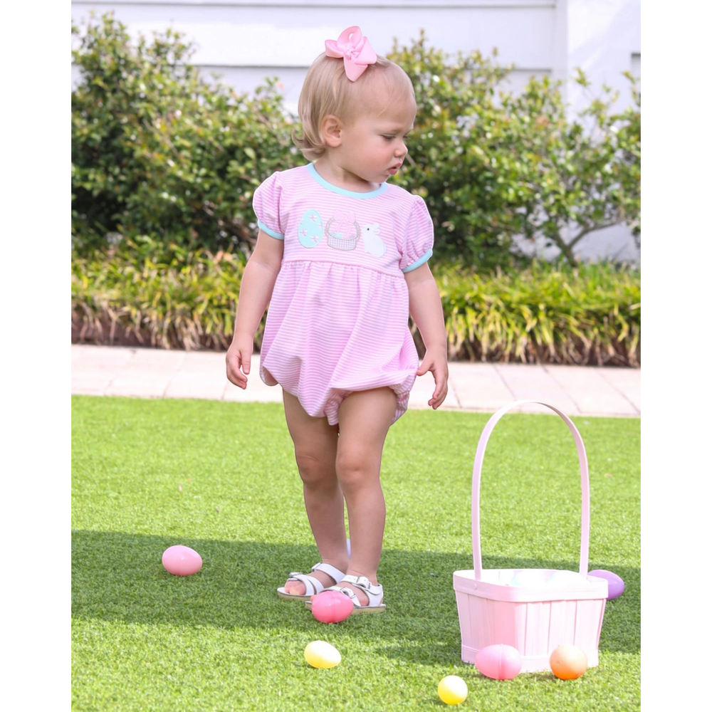 Child in a pink bubble playing with Easter eggs on grass