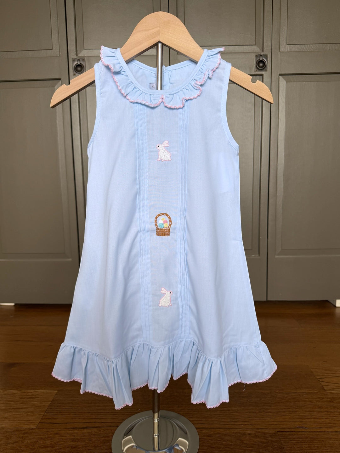 Light blue dress with bunny and carrot design on a wooden hanger against a neutral background